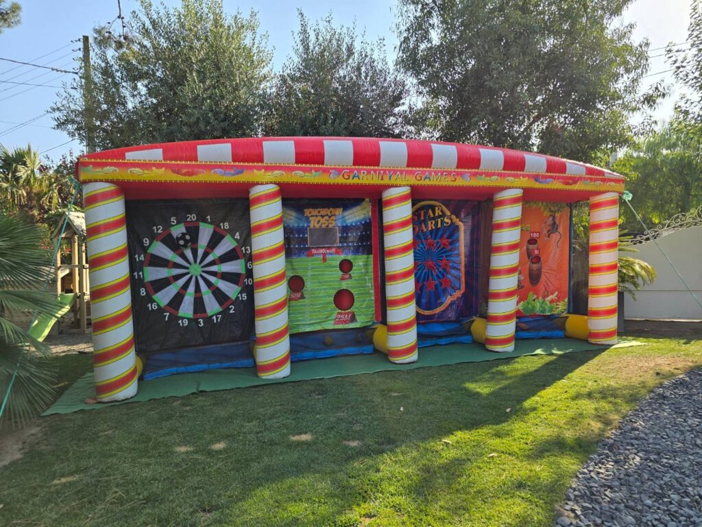 Stand gonflable de kermesse avec 4 jeux d’adresse alignés : cible, lancer, fléchettes.