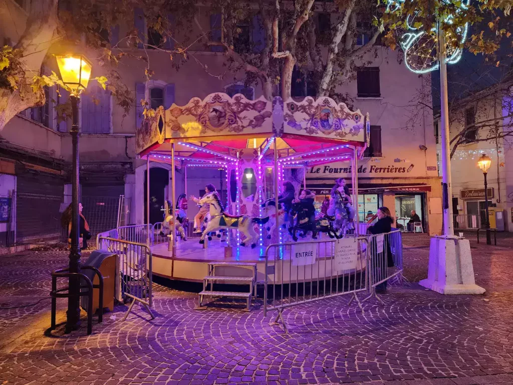 Carrousel illuminé la nuit sur une place de centre-ville décorée.