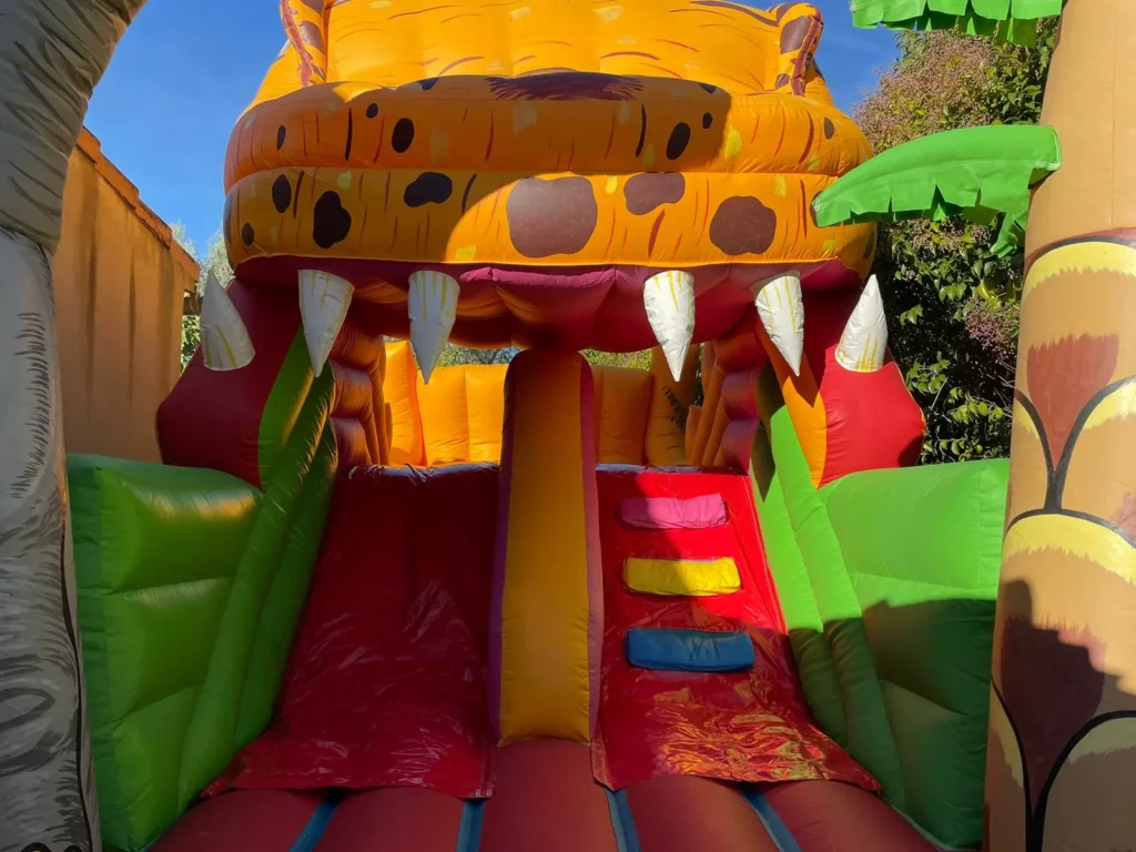 Entrée du toboggan gonflable dinosaure avec décor réaliste et coloré.